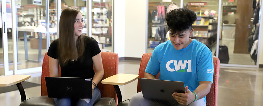 CWI students smiling while working on their laptops.